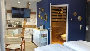 Et hotelværelse med seng, skrivebord, fjernsyn, brusebad og badeværelse.