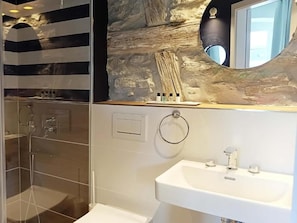 Un baño moderno con cabina de ducha de vidrio, un lavabo blanco y un fondo de pared de piedra.