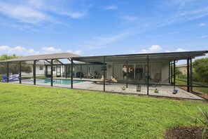 Ein modernes Haus mit überdachter Terrasse, Schwimmbad und gepflegtem Rasen.