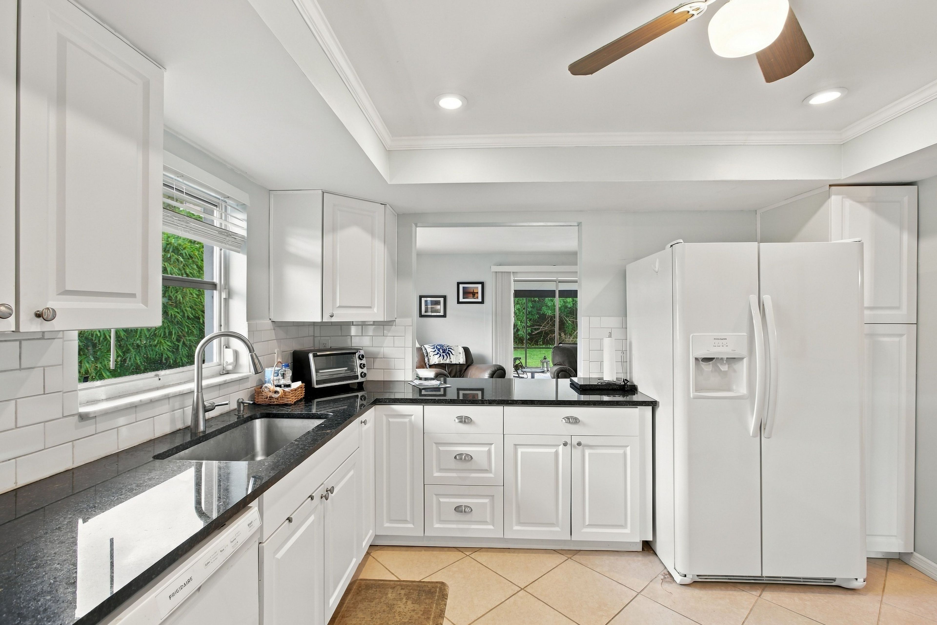 Una cocina moderna con muebles blancos, horno empotrado, refrigerador y ventana con persianas.