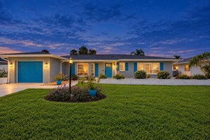 A two-story house with a blue garage door, a well-maintained lawn, and a landscaped garden with potted plants. - Rotonda Getaway with Heated Pool & Lanai (Rotonda West)
