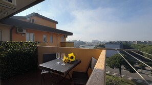 Ein Balkon mit Tisch, Stühlen und einem Weinglas, mit Blick auf eine Stadtlandschaft.
