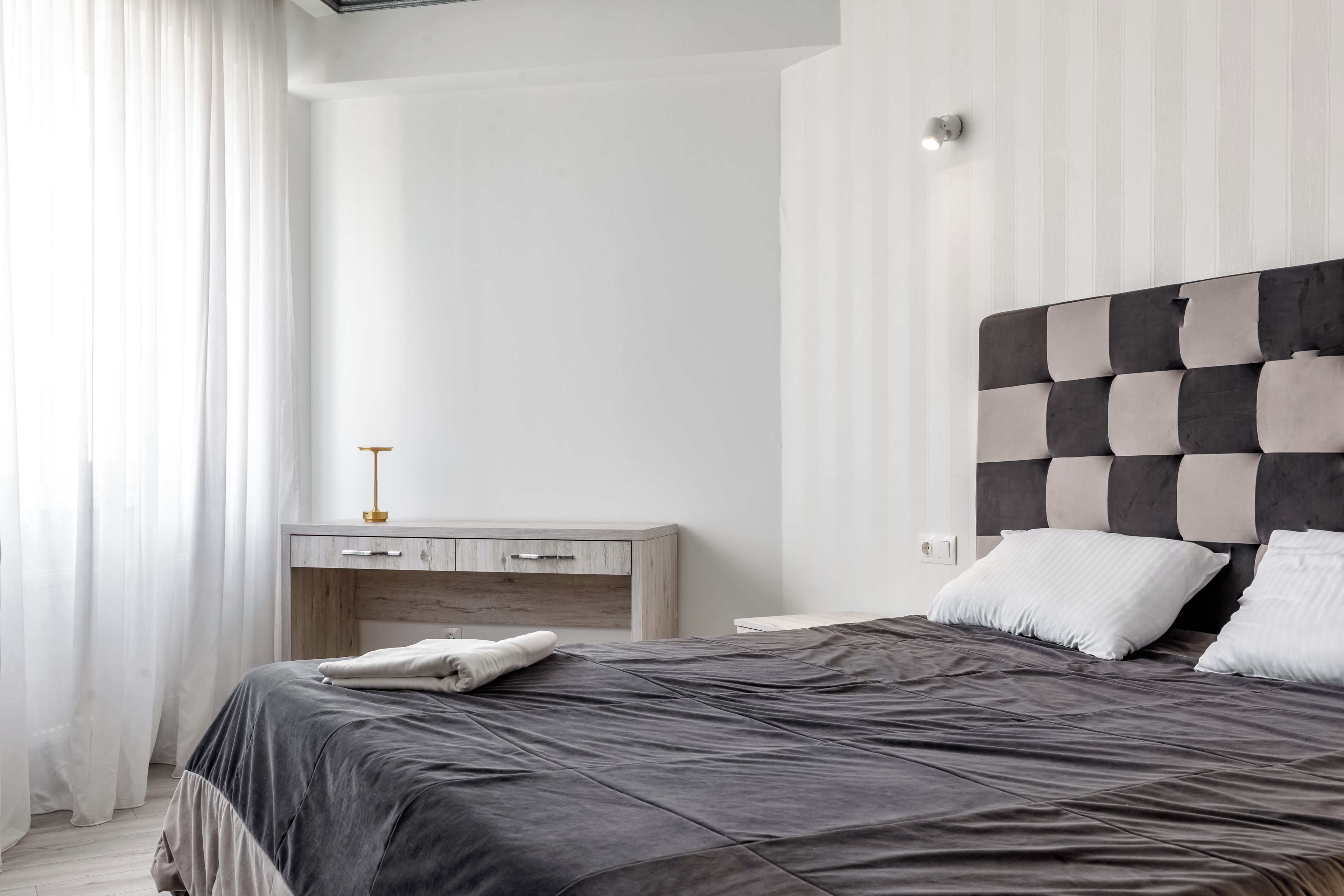 A modern bedroom with a bed, a nightstand, and a wall-mounted light.