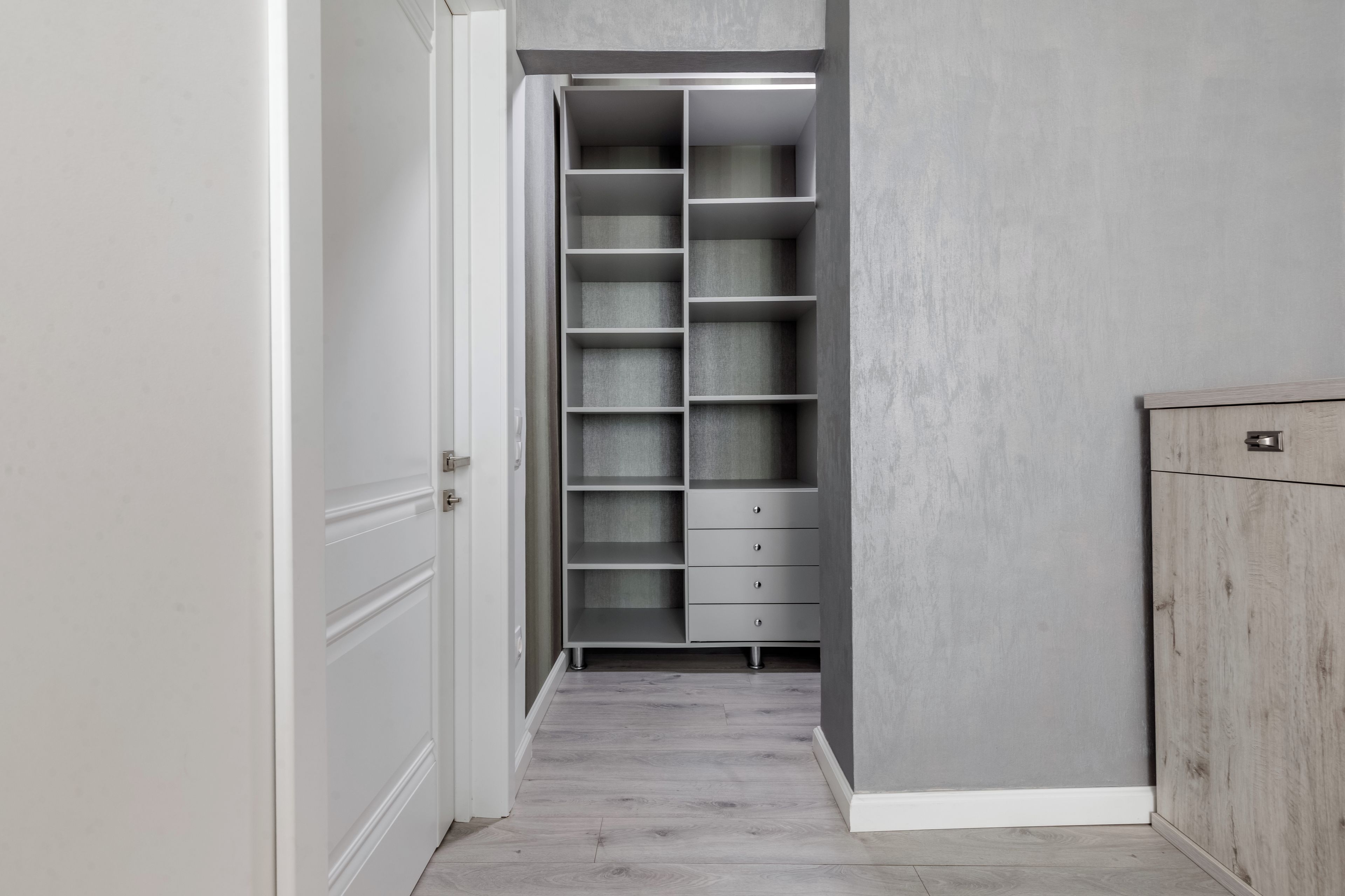A narrow hallway with a built-in closet featuring multiple shelves and drawers.