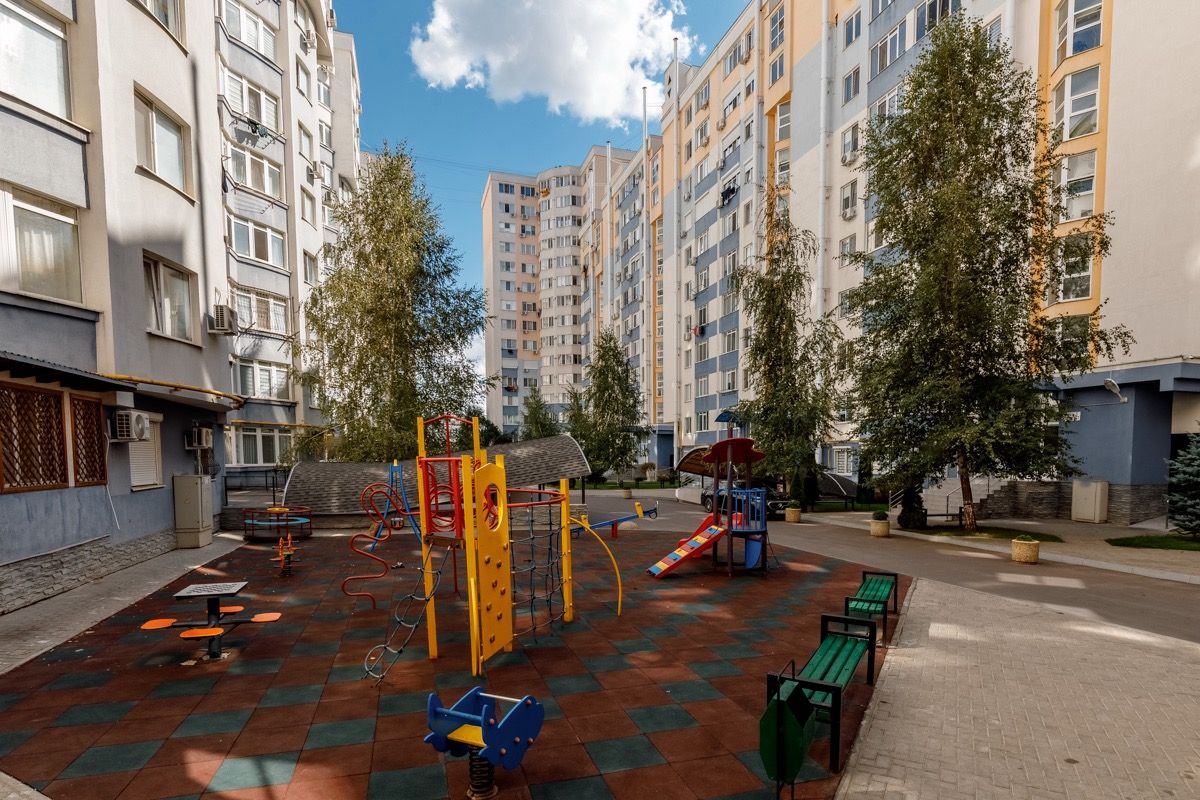 Área de lazer infantil com estruturas de recreação e bancos, rodeada por edifícios de apartamentos.