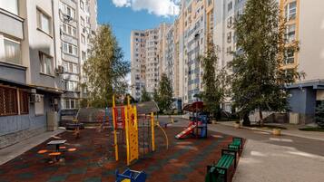 Área de lazer infantil com estruturas de recreação e bancos, rodeada por edifícios de apartamentos.