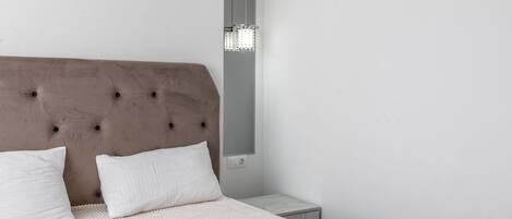 A bedroom with a tufted headboard, a white bedspread, and a bedside table with a lamp.