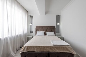 A bedroom with a large bed, a nightstand, a wall-mounted lamp, and sheer curtains. - Spacious 2BR, 9th Floor View, Bright & Modern (Chișinău)