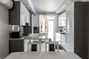 A modern kitchen with white cabinetry, a dining table, and a window with sheer curtains.