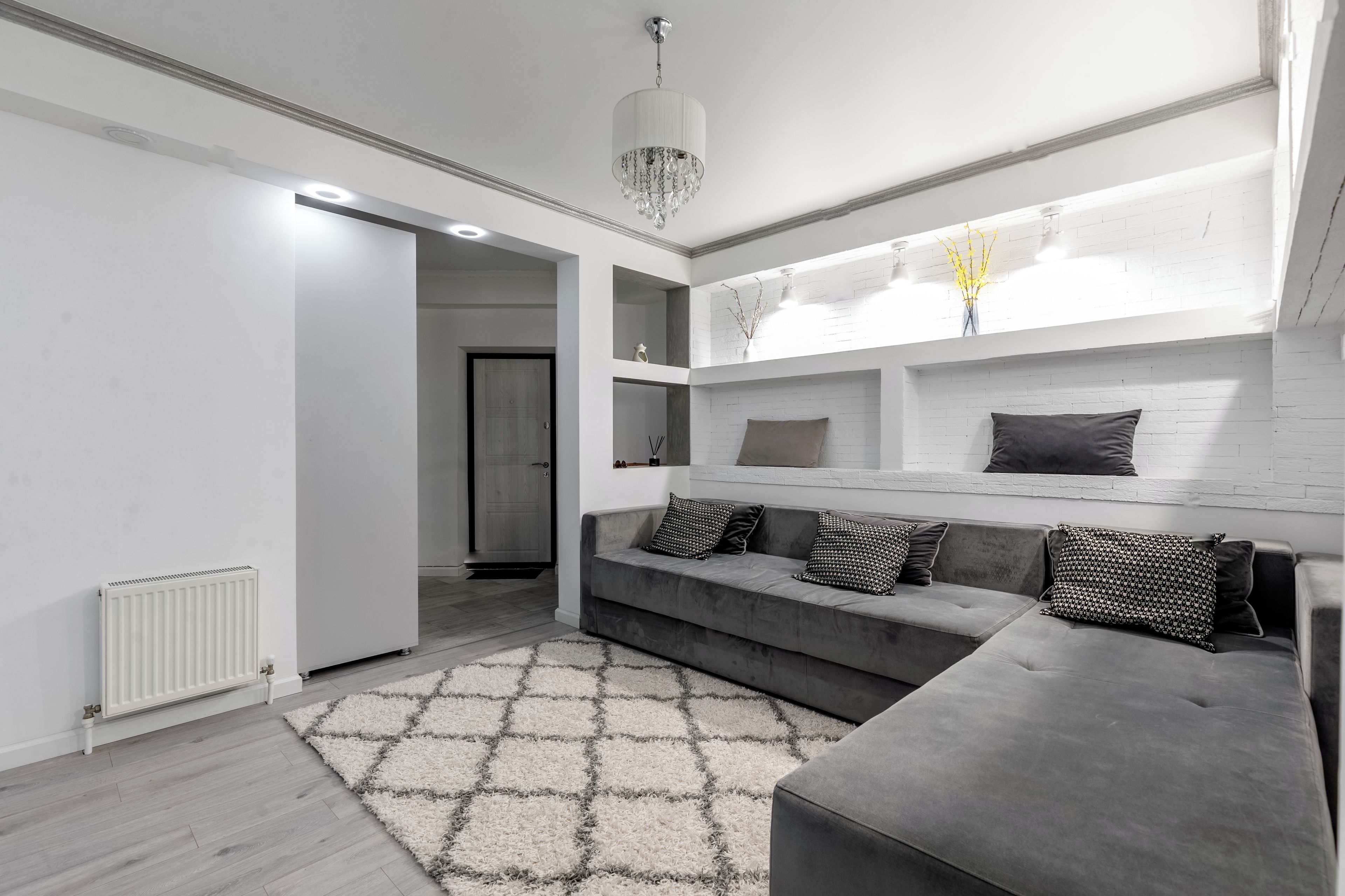 A modern living room with a grey sofa, patterned cushions, a white radiator, and a geometric rug.