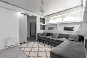 A modern living room with a grey sofa, patterned cushions, a white radiator, and a geometric rug. - Spacious 2BR, 9th Floor View, Bright & Modern (Chișinău)
