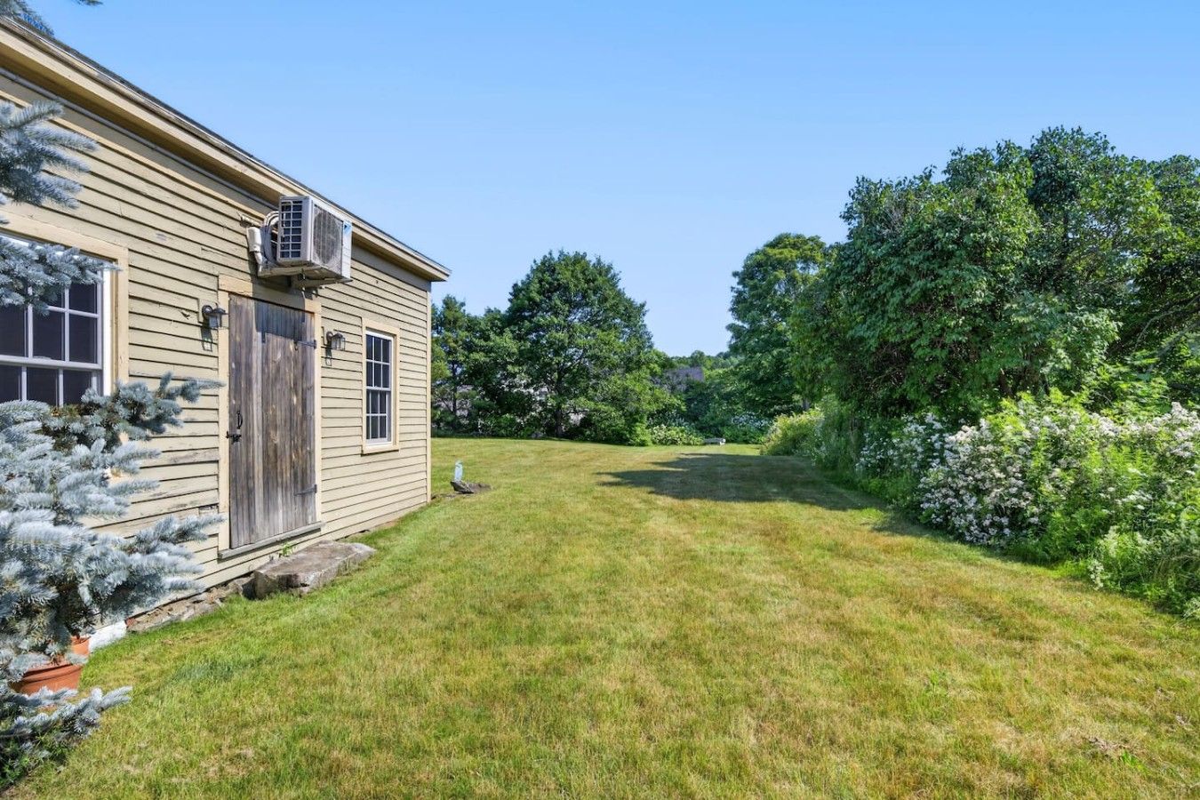 Une maison avec un jardin devant, une porte en bois et un appareil de climatisation.