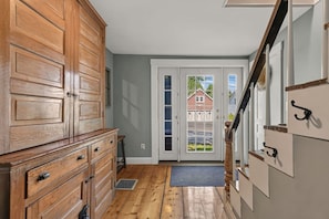 A hallway with a wooden cabinet, a door leading outside, and a staircase. - Stunning Waterfront Farmhouse (Belfast)