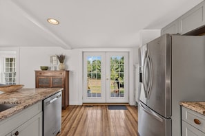 A kitchen with a wooden floor, a stainless steel refrigerator, and a double door leading to an outdoor area. - Stunning Waterfront Farmhouse (Belfast)