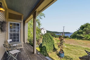 A covered porch with a table and chairs, a potted plant, and a view of a lake and a bridge. - Stunning Waterfront Farmhouse (Belfast)