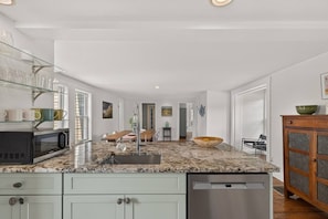A modern kitchen with a granite countertop, a dishwasher, and a dining area with a wooden table and chairs. - Stunning Waterfront Farmhouse (Belfast)