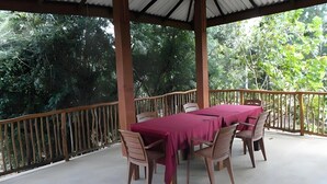 An outdoor covered dining area with a table and chairs, surrounded by a wooden railing and a view of dense greenery. - Echo Lodge (Habarana)