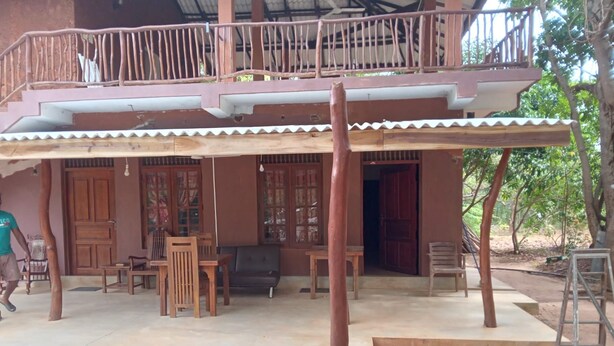 A two-story building with a balcony, wooden furniture, and a concrete floor. - Echo Lodge (Habarana)