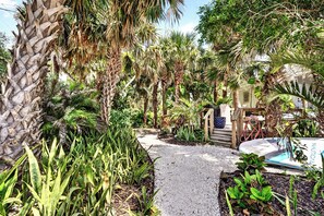 A pathway surrounded by lush greenery and palm trees, leading to a building with a visible door and windows. - 2 BR/2 BA Beach Front Suite-Kayaks-SUPs-Bikes-Pets (Englewood)