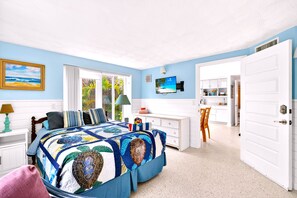 Een slaapkamer met een bed, een bureau, een stoel, een televisie en een deur naar een badkamer.