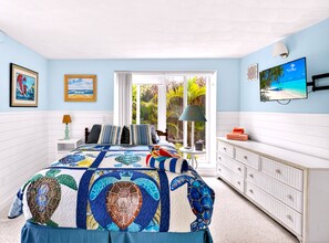 A bedroom with a large bed, a dresser, a television, and a window with a view of greenery. - 2 BR/2 BA Beach Front Suite-Kayaks-SUPs-Bikes-Pets (Englewood)