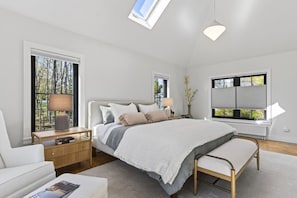 A modern bedroom with a large bed, bedside tables, a bench, and a skylight.
