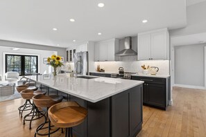 A modern kitchen with a large island, bar stools, and a view to the living area.