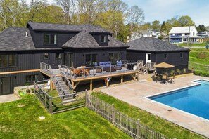 A modern two-story house with a deck, outdoor seating, and a swimming pool.