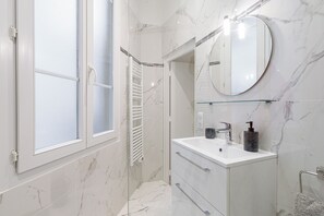 Un bagno moderno con box doccia in vetro, un mobile lavabo bianco con specchio e una parete rivestita in marmo.