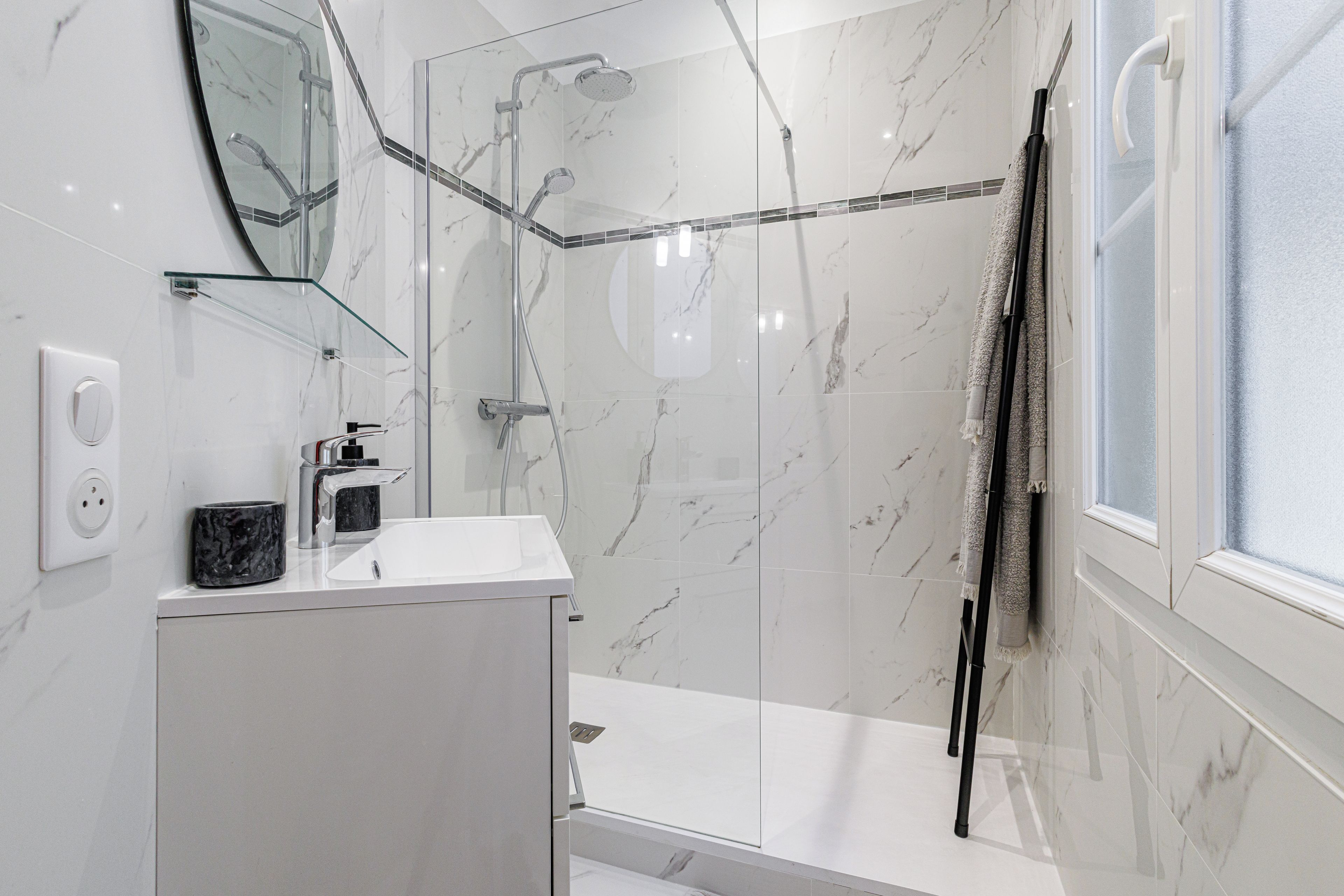 Une salle de bain moderne avec une douche à parois de verre, un lavabo blanc et un miroir.