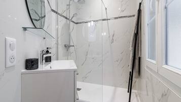 Un baño moderno con cabina de ducha de vidrio, un lavamanos blanco y un espejo.
