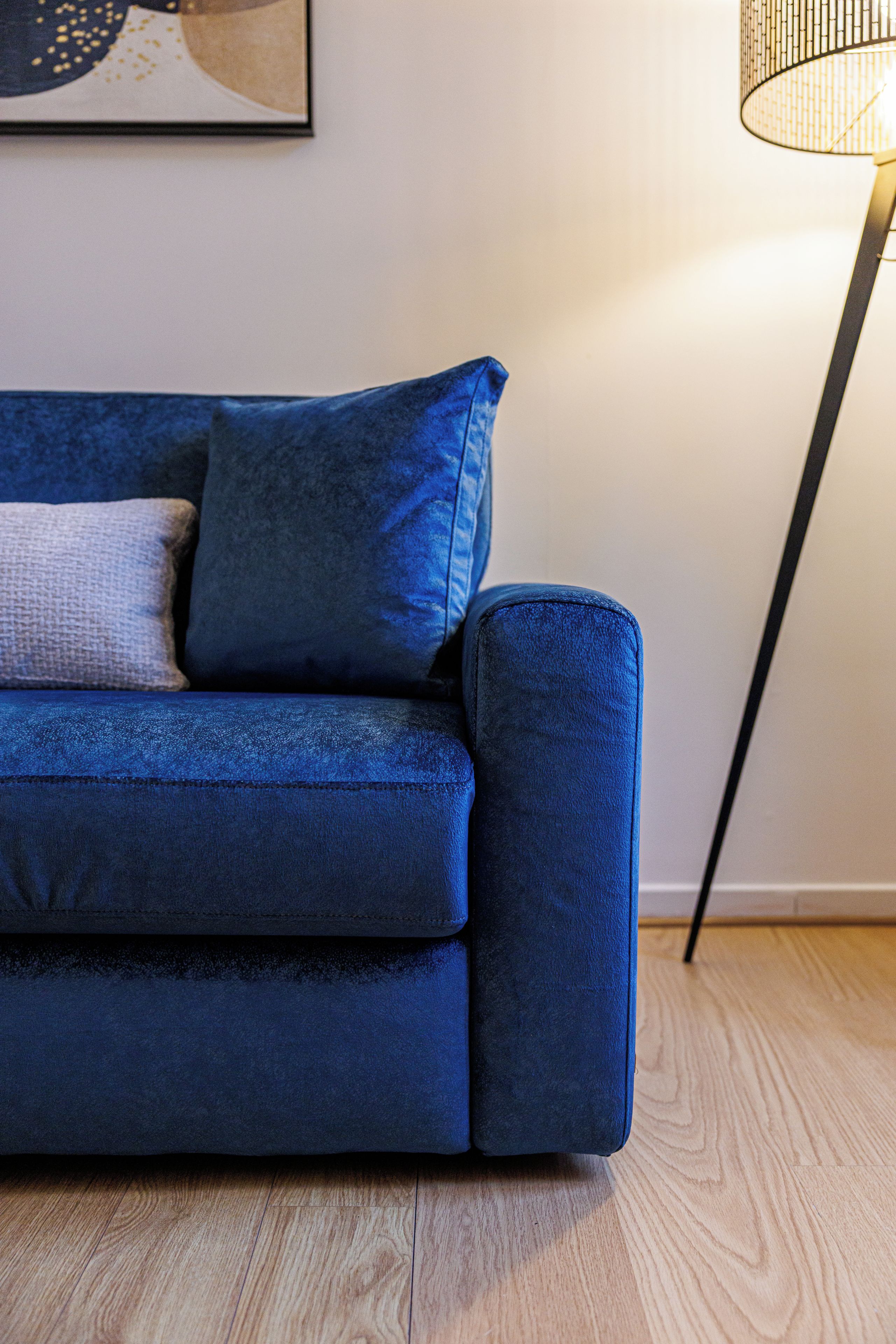 Un canapé bleu avec un coussin et une lampe, dans une pièce dont le sol est recouvert de parquet.