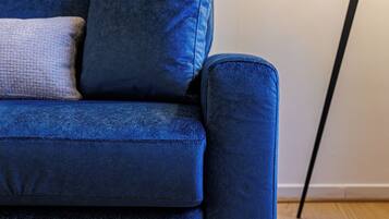 Un canapé bleu avec un coussin et une lampe, dans une pièce dont le sol est recouvert de parquet.