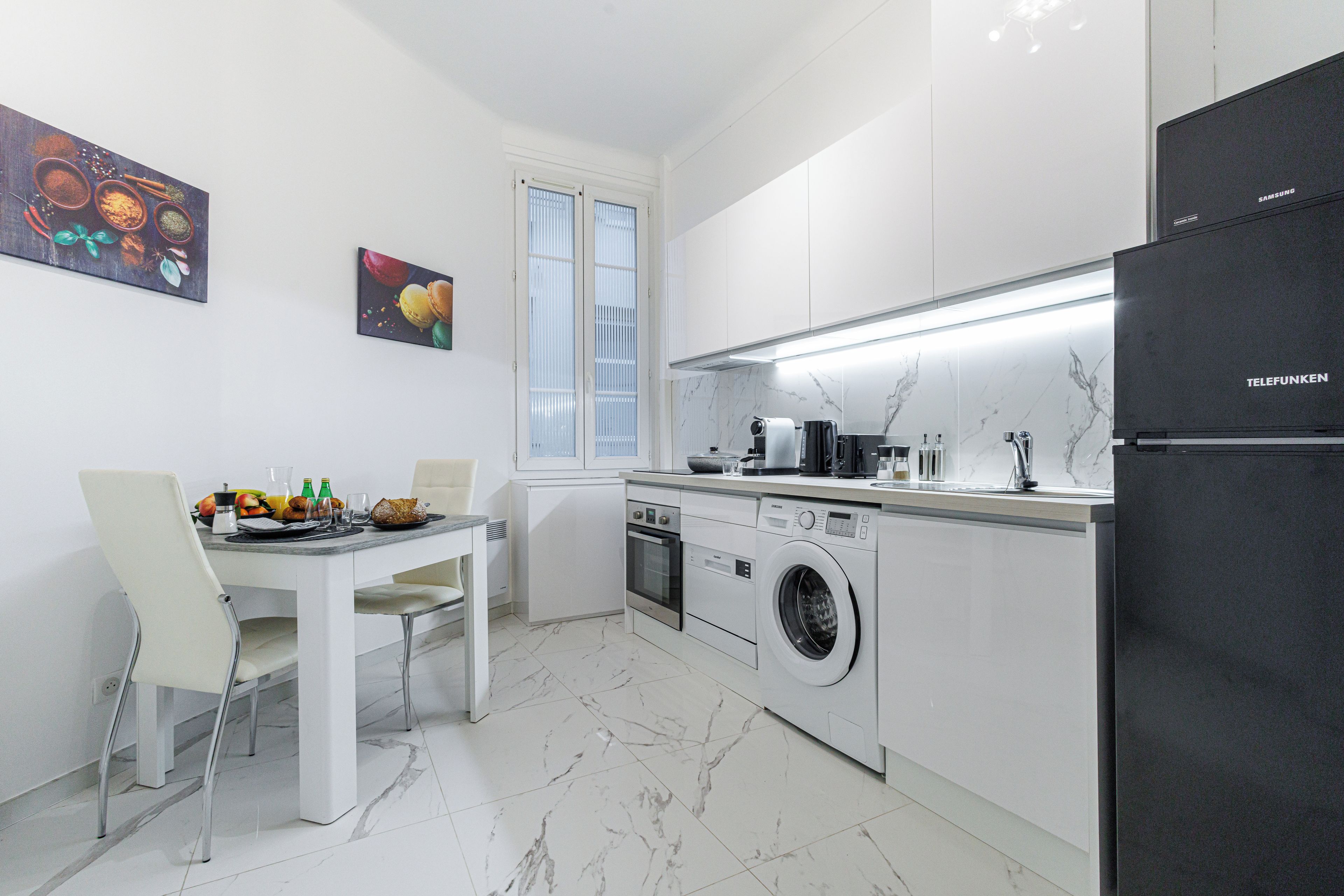 A modern kitchen with a washing machine, a refrigerator, and a dining area with chairs and a table.