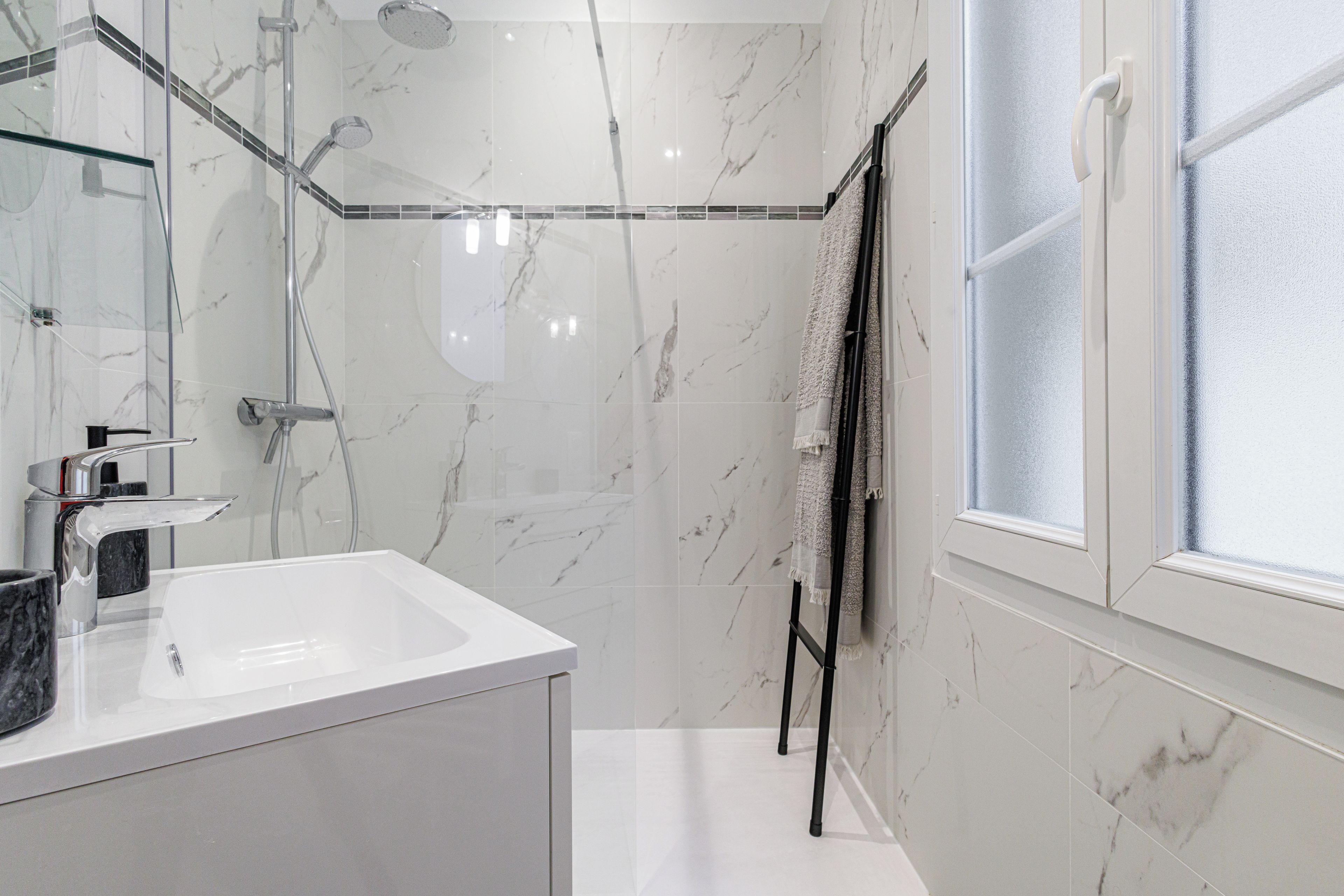 Une salle de bain moderne avec une douche à parois de verre, un lavabo blanc et un porte-serviettes.