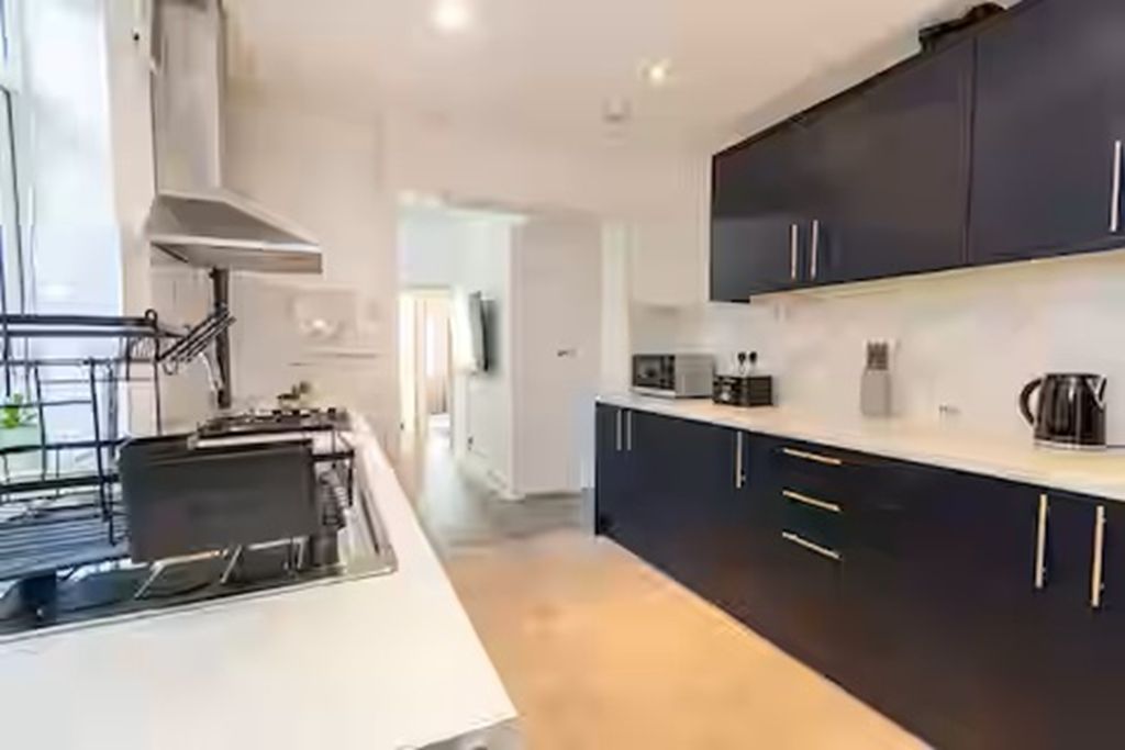 A modern kitchen with dark cabinetry, a white countertop, and a stainless steel range hood.