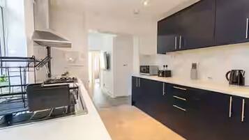 A modern kitchen with dark cabinetry, a white countertop, and a stainless steel range hood.
