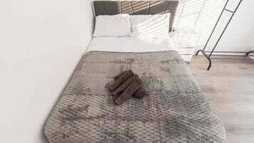 A bed with a textured blanket and folded towels, a headboard, and a window with blinds.