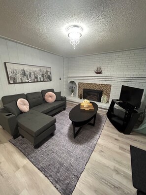 A living room with a sofa set, a fireplace, a television, and a chandelier.