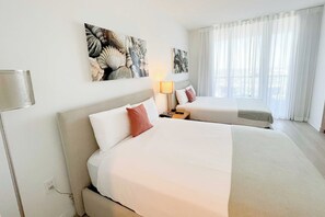A hotel room with two beds, a nightstand, a lamp, and artwork on the walls. - Cozy Chic Studio Pininfarina Design/ Resort Style (Hallandale Beach)