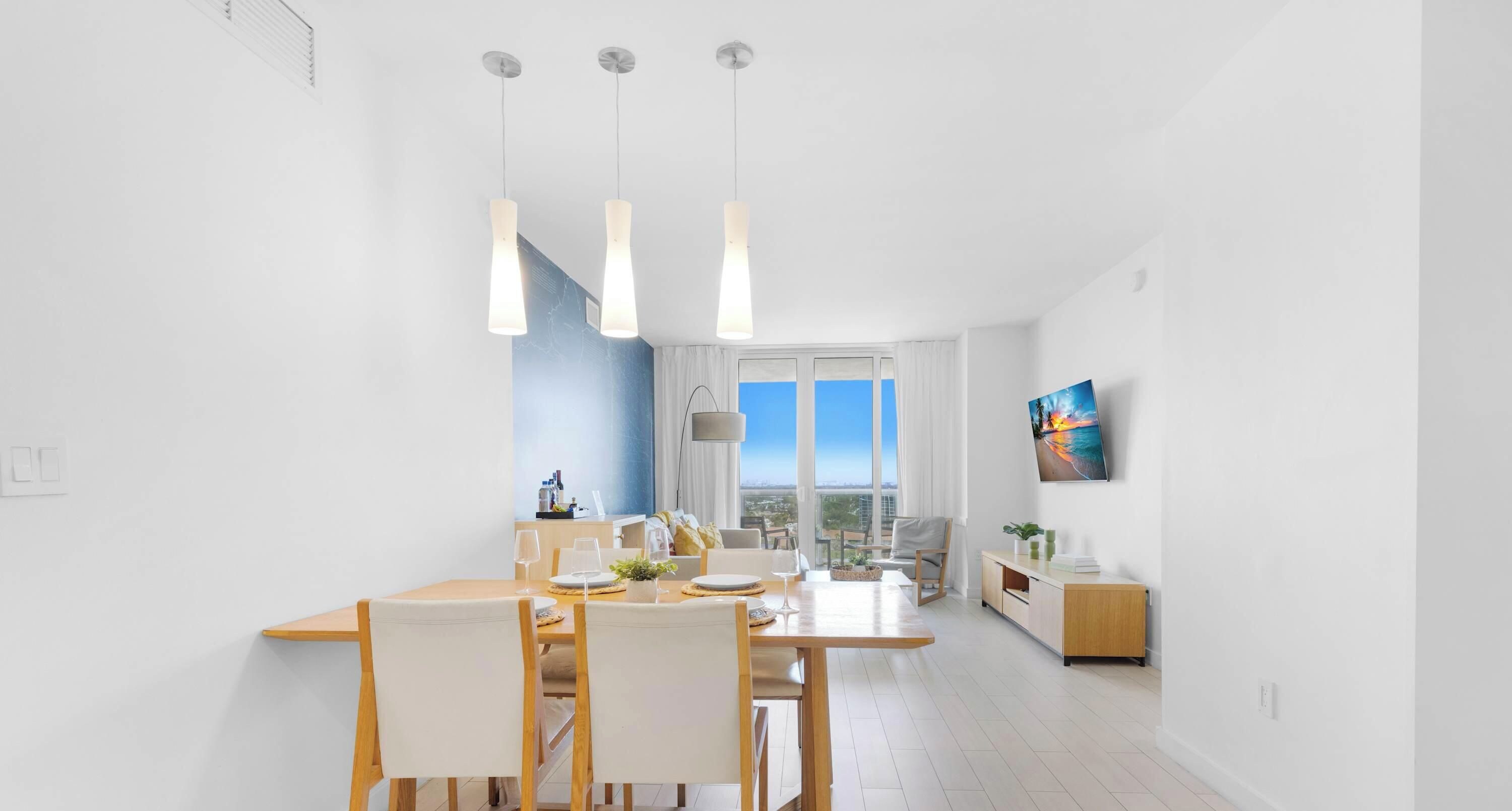 Una habitación de hotel moderna con zona de comedor, un ventanal con vistas a la ciudad y un cuadro en la pared.