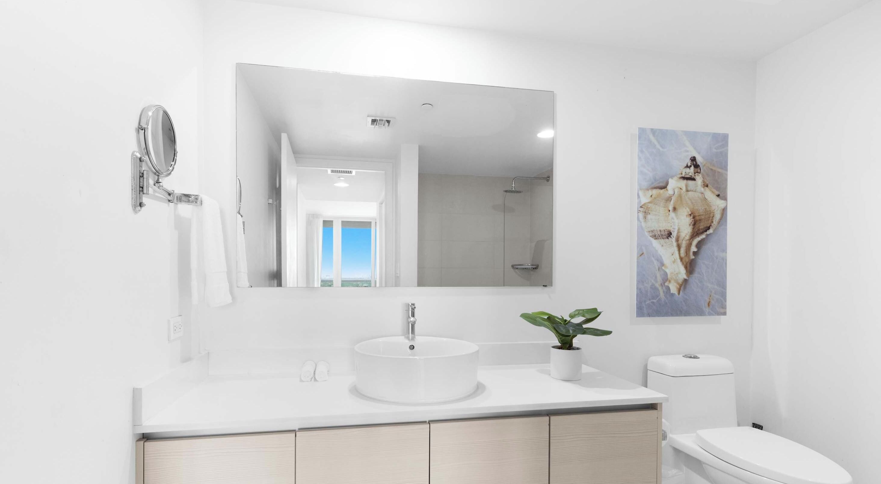 Un bagno moderno con lavandino, specchio e vaso in ceramica bianchi.