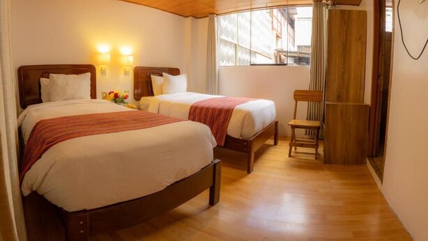 A hotel room with two beds, a wooden floor, a chair, and a window with curtains. - Seven Machupicchu (Aguascalientes)