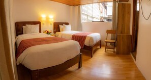 Een hotelkamer met twee bedden, een houten vloer, een stoel en een raam met gordijnen.