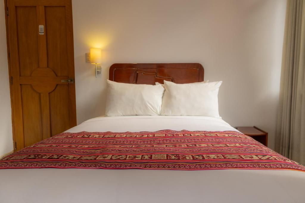 Una habitación de hotel con puerta de madera, cama con ropa de cama blanca y una manta decorativa.