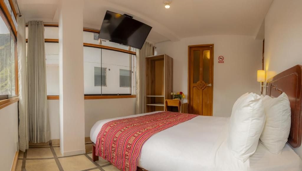 Una habitación de hotel con una cama, televisión montada en la pared, un armario y una puerta.