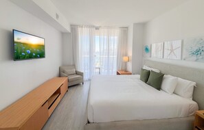 A hotel room with a bed, a chair, a TV, a lamp, and artwork on the walls. - Modern APT w/ Panoramic Intracoastal 2BR High Floor (Hallandale Beach)