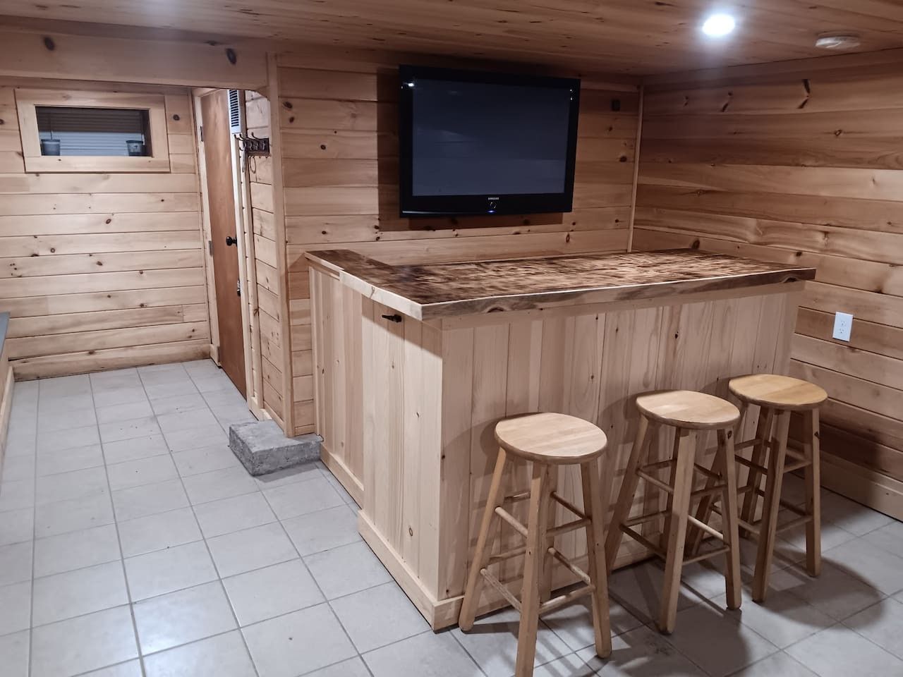 Interior em madeira com área de bar, banquetes e uma televisão na parede.