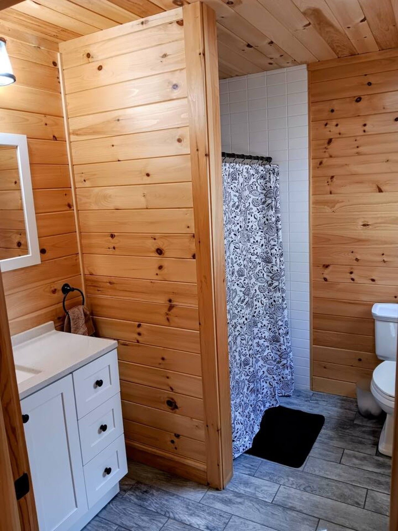 Un baño con paneles de madera, un lavamanos blanco, un perchero y una cortina de ducha estampada.