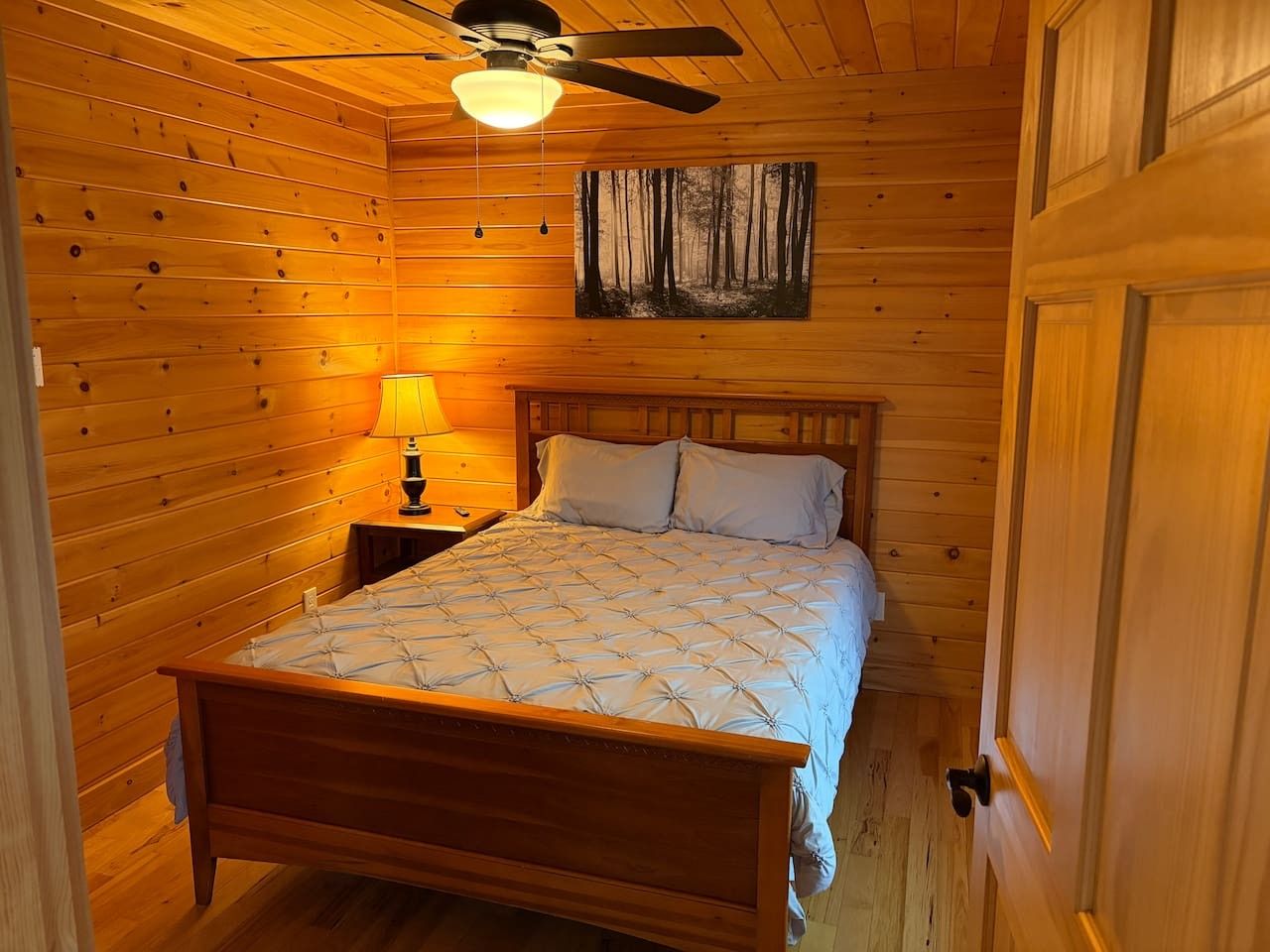 A wooden-paneled room with a bed, a nightstand, a lamp, and a ceiling fan.